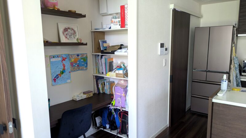 リビング側から見た造作デスクと隣接収納棚の全景。ランドセル・教科書・習い事バッグが各段に収まっている