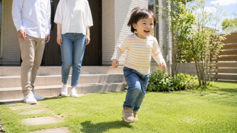 戸建て住宅の庭で遊ぶ子供と見守る夫婦。住宅ローンで家を建てた家族の実例