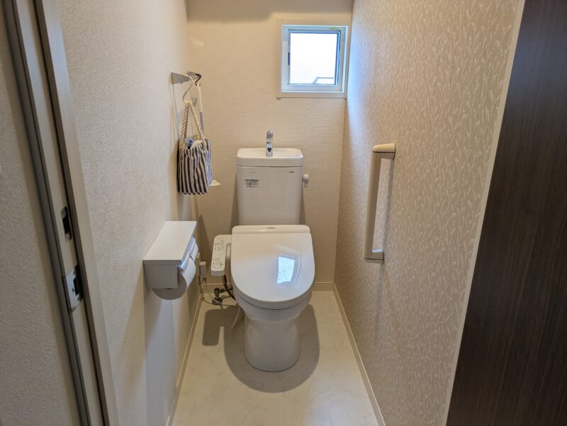 1階トイレの全景。便器、タンク上部の手洗い、窓、手すりが見える