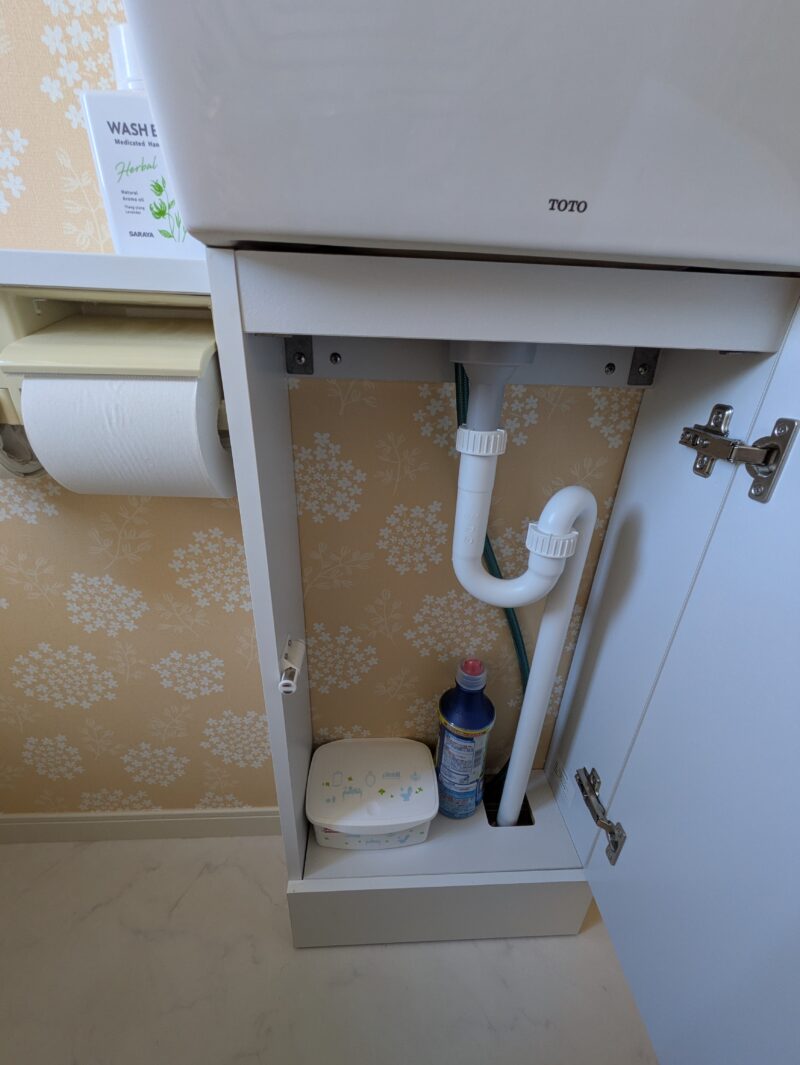 2階トイレの手洗い器の下の収納。扉を開けると、配管の横に洗剤や小物を置いている